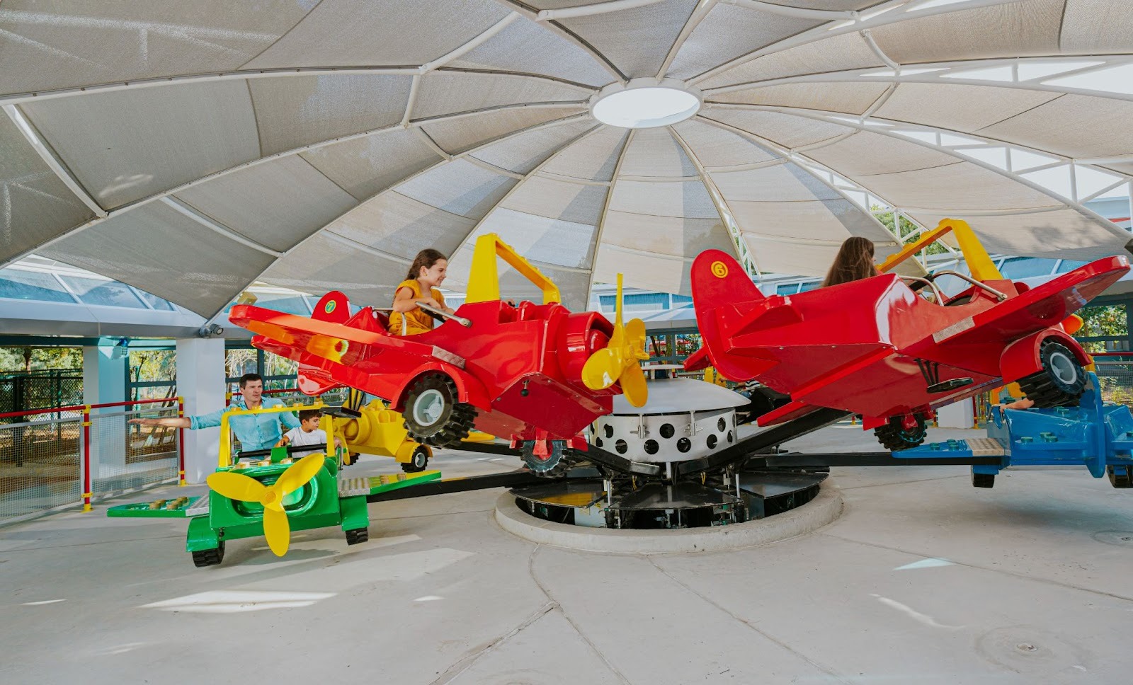 Children enjoy a colorful plane-themed ride under a large canopy.