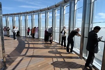 People standing on a glass observation deck at the top of Burj Khalifa, overlooking the city skyline.