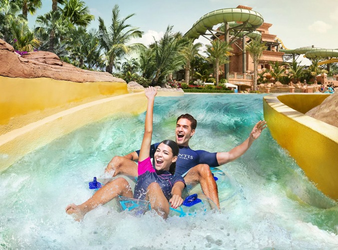 Two people joyfully riding a colorful water slide at a vibrant water park on a sunny day.