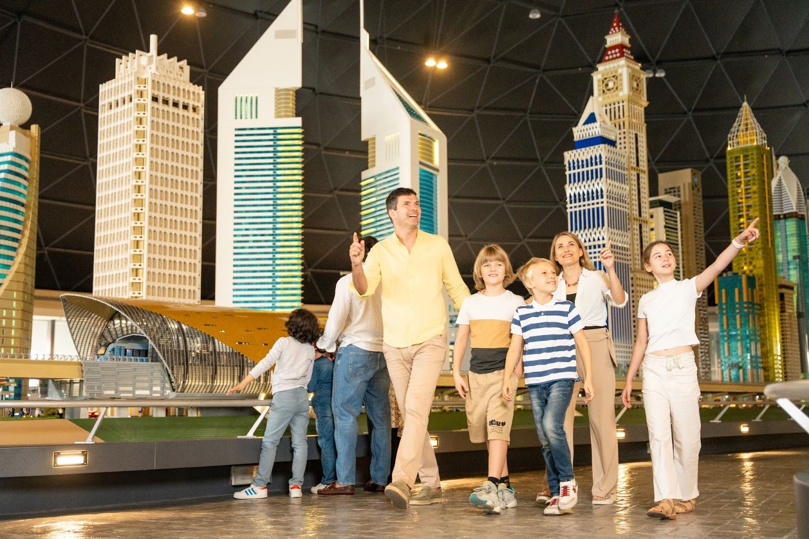A family of six admires tall, colorful skyscraper models indoors