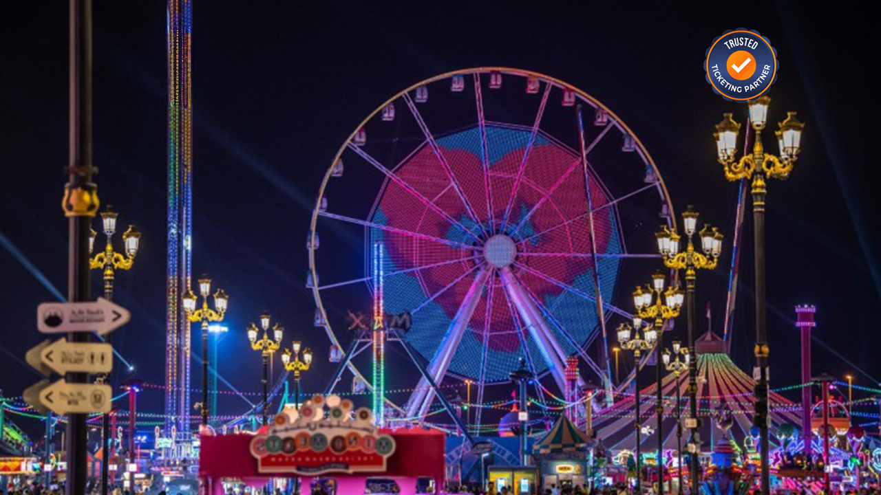 A vibrant night-time carnival scene with a large, illuminated Ferris wheel displaying colorful lights.