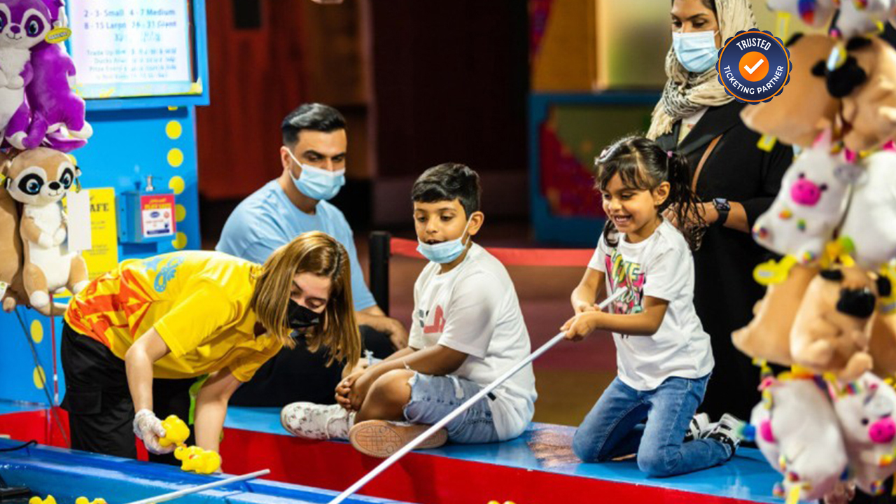 Children play a duck pond game at a fair, guided by an attendant. They look happy and engaged.